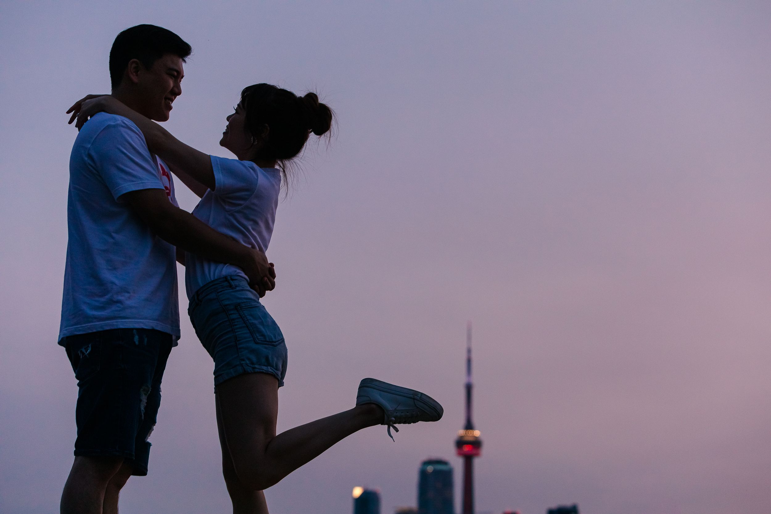 A couple dances together on a rooftop terrace against a city skyline at sunset.