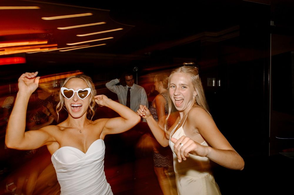 Wedding guests dance and celebrate on a dimly lit dance floor during an evening reception.