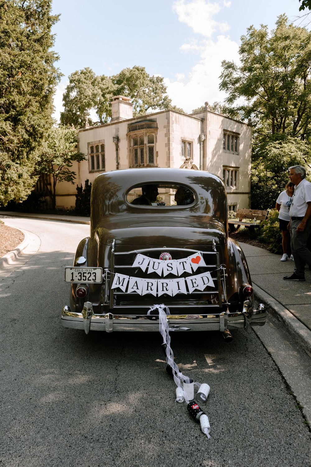 Classic vintage car decorated with white ribbons and 'Just Married' signage parked on a street for a wedding celebration.
