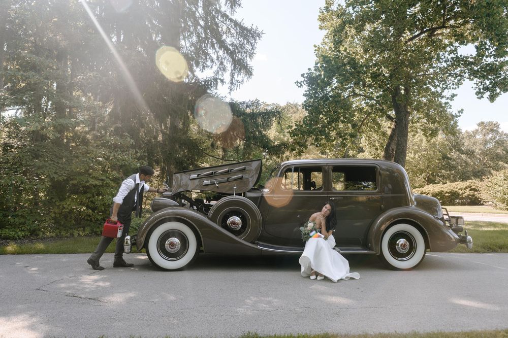 Vintage car parked on a garden path during a wedding photoshoot with sunlight streaming through trees.