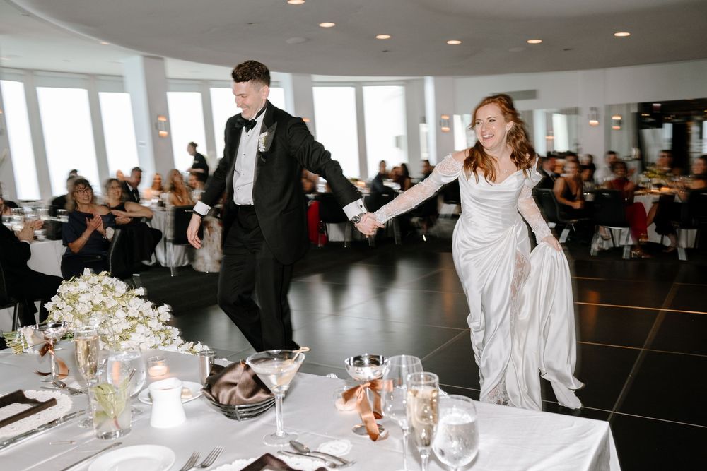 Bride and groom make grand entrance at elegant wedding reception, bride in white gown holding groom's hand.