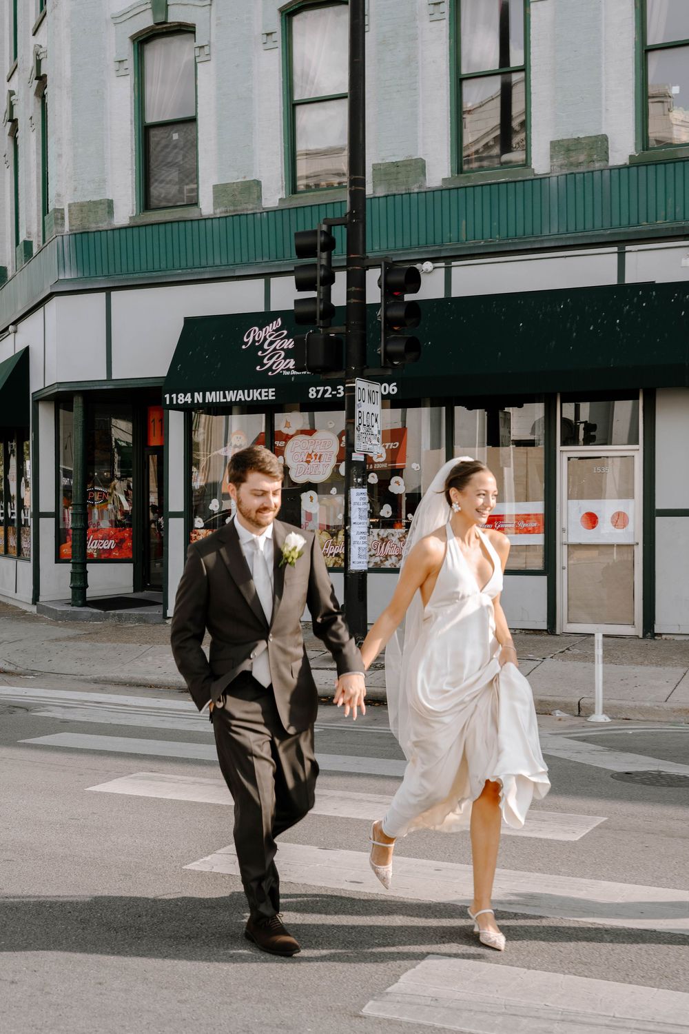 A couple in formal wedding attire playfully runs and dances across a city crosswalk in a sequence of photos.
