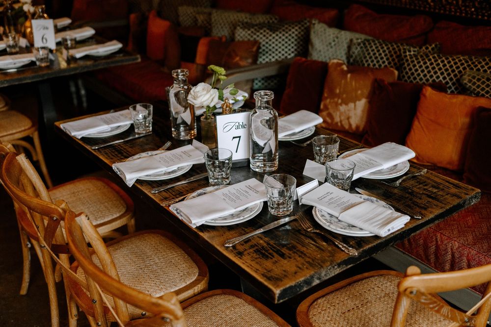 Restaurant table settings with white plates and napkins arranged on dark wooden tables in a cozy dining room.