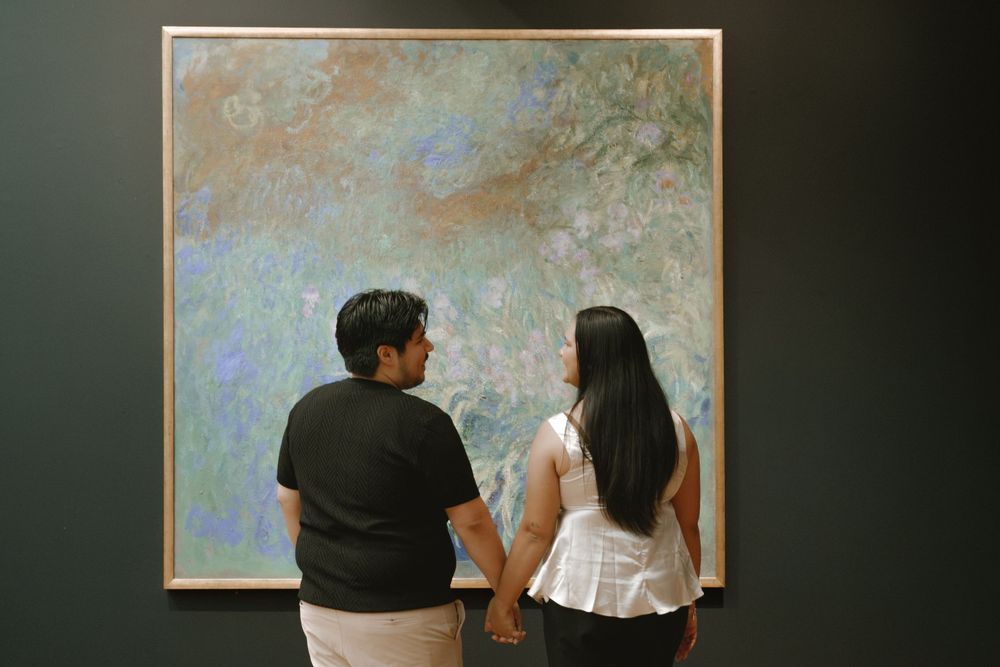 Couple holding hands viewing a large impressionist painting in an art museum gallery.