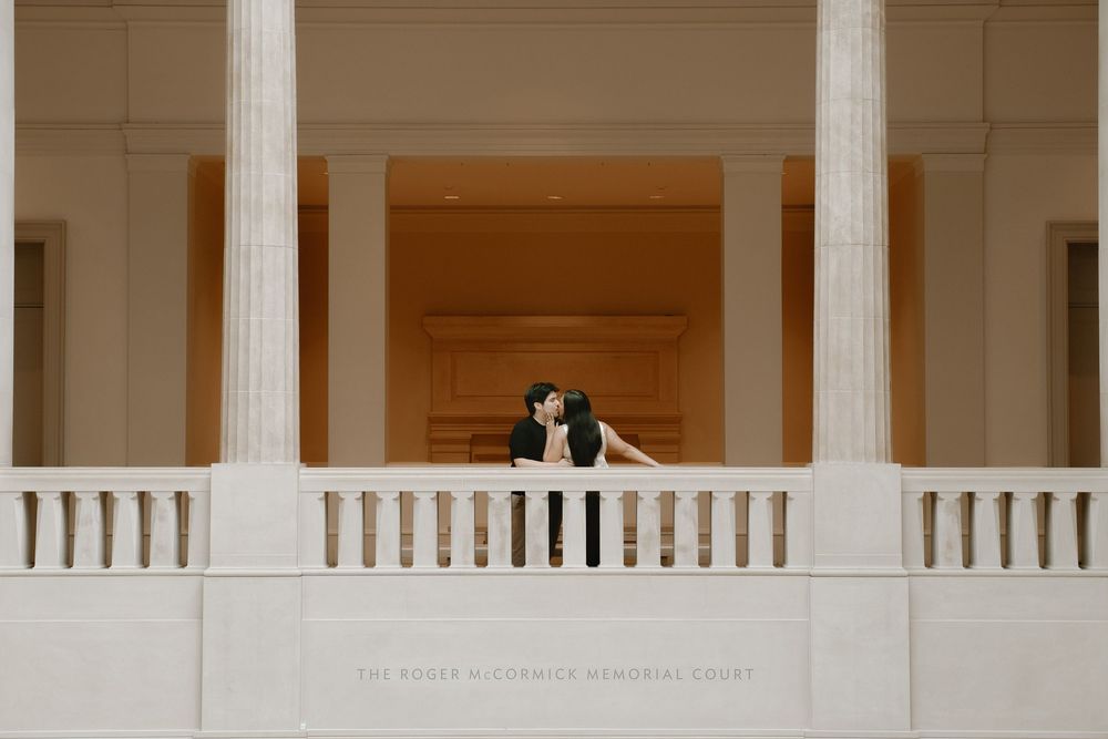 Couple sharing a romantic kiss on a grand balcony with tall white columns at the McKee McCormick Memorial Chapel.