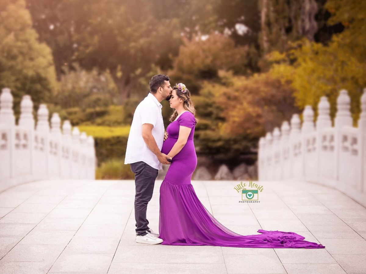 A romantic couple embraces in a studio setting, with the woman wearing an elegant navy blue ruffled gown.