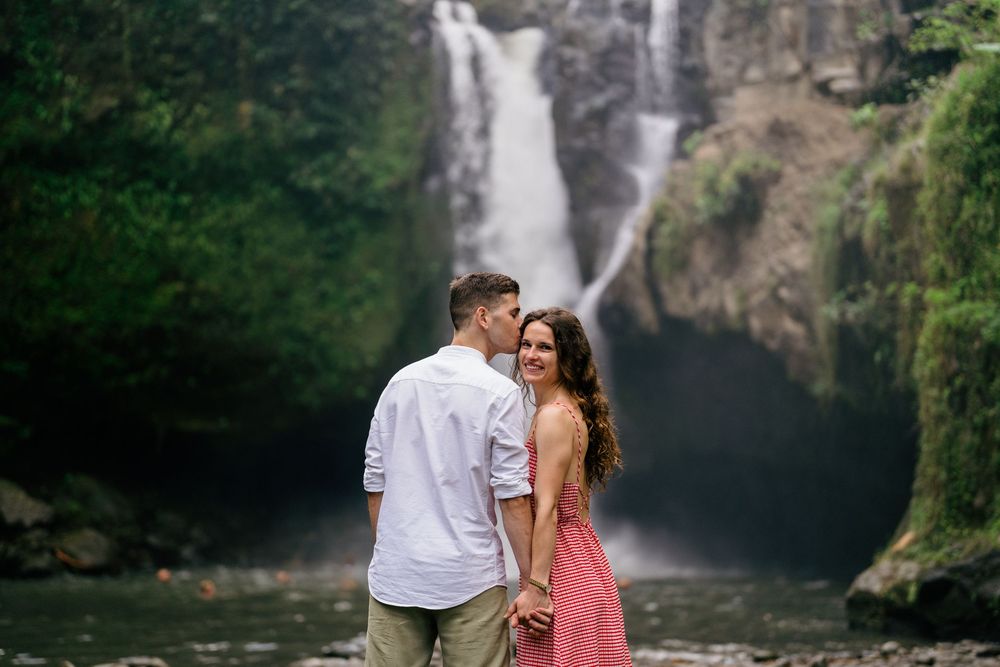 Couple embracing near scenic waterfall with rocky foreground.