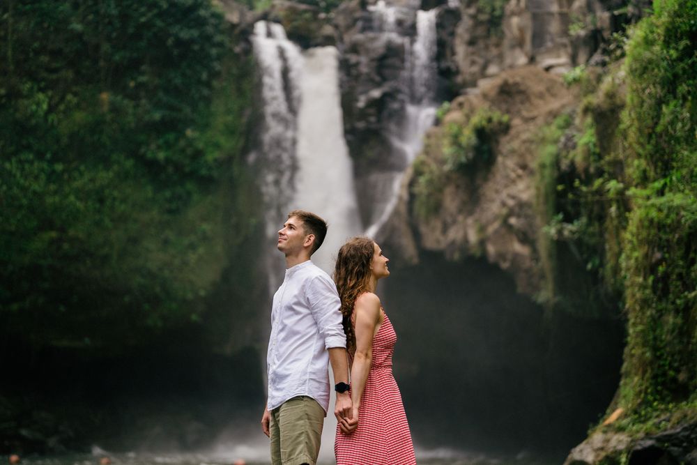 Couple enjoying scenic waterfall view while standing on rocks.