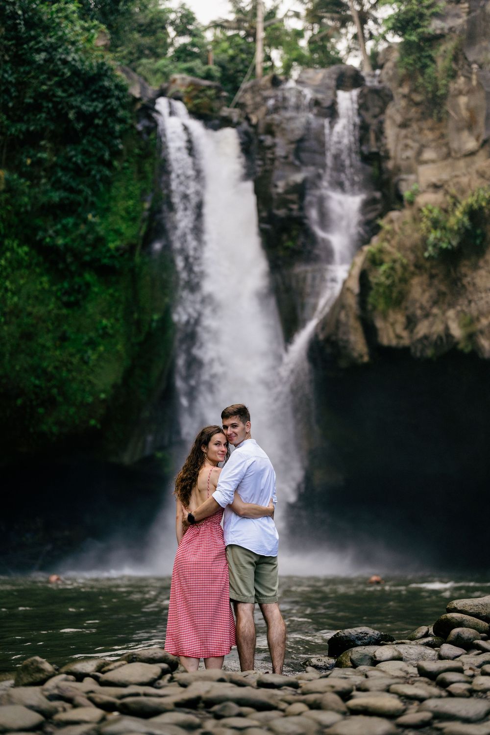 A romantic moment captured between two people by a scenic waterfall and rocky shoreline.