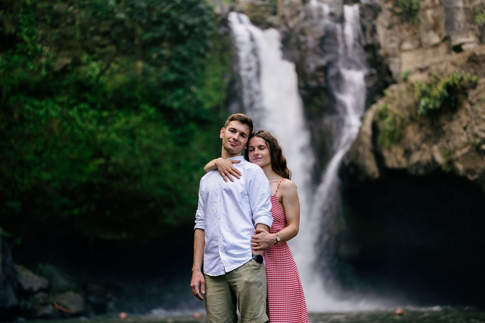 A couple shares an intimate embrace near a cascading waterfall surrounded by nature.