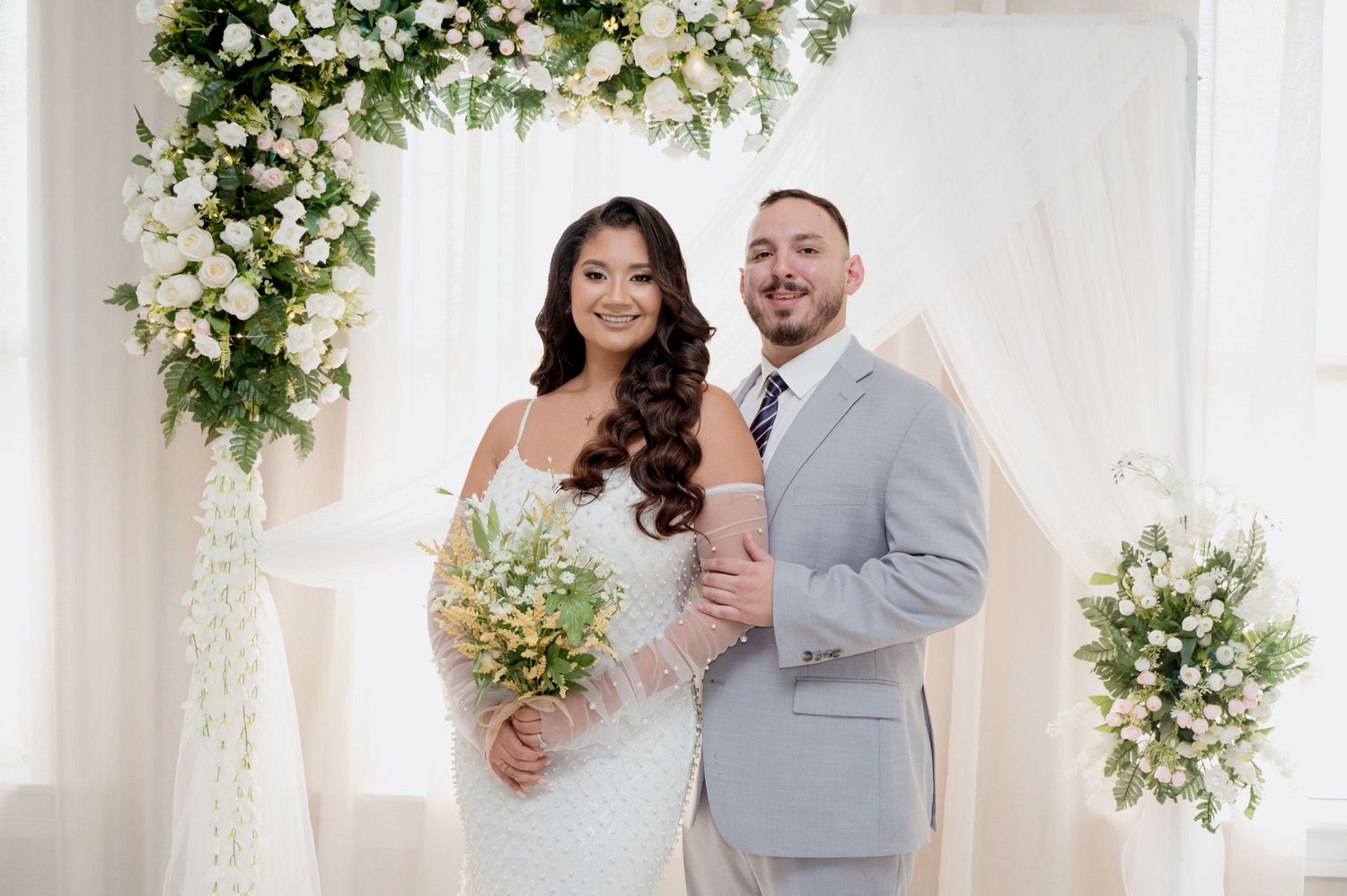 Romantic wedding portraits showing couples posing together against white floral backdrop during celebration ceremony.