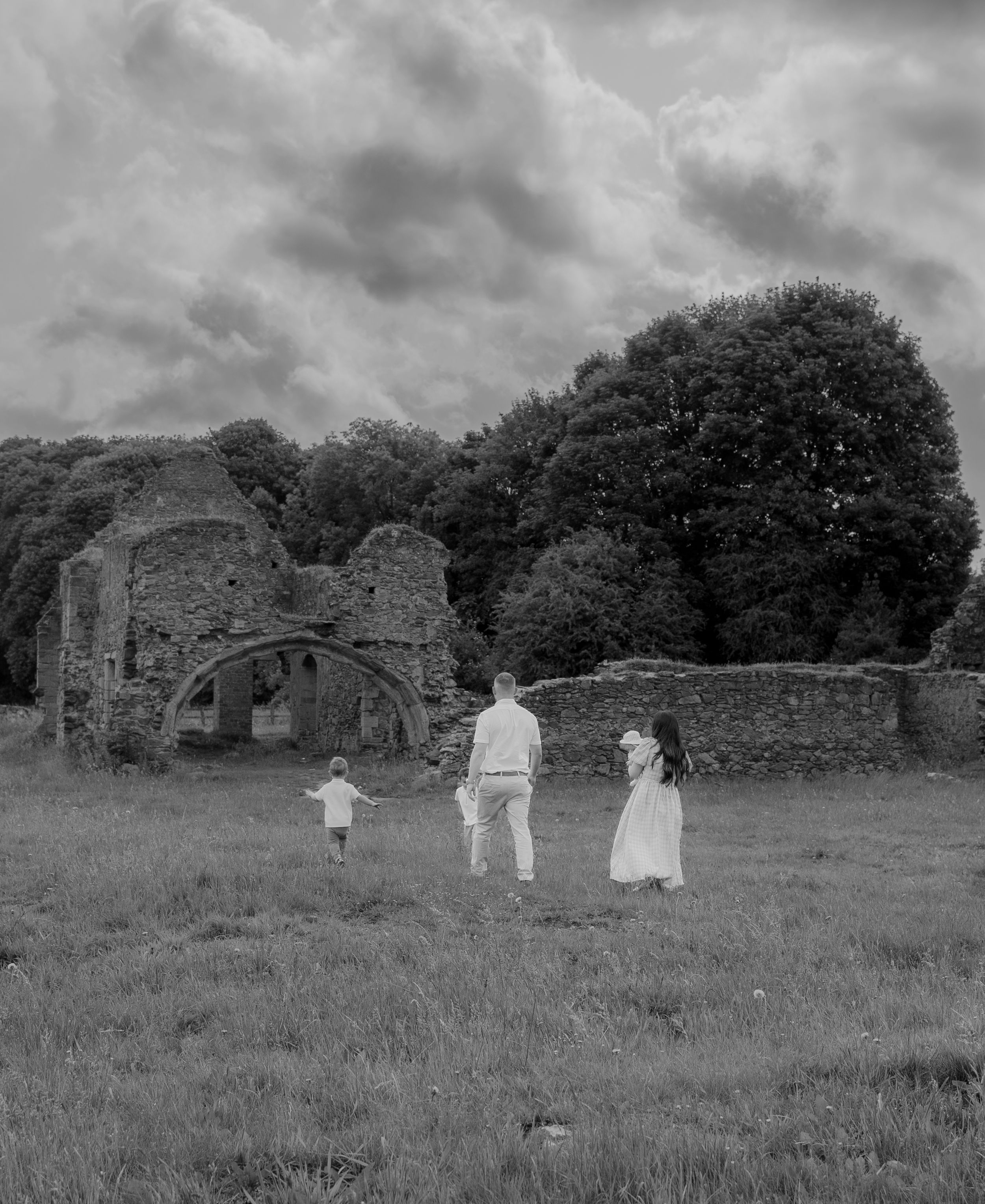 A sequence of black and white photographs showing people walking through a grassy field near old stone ruins.