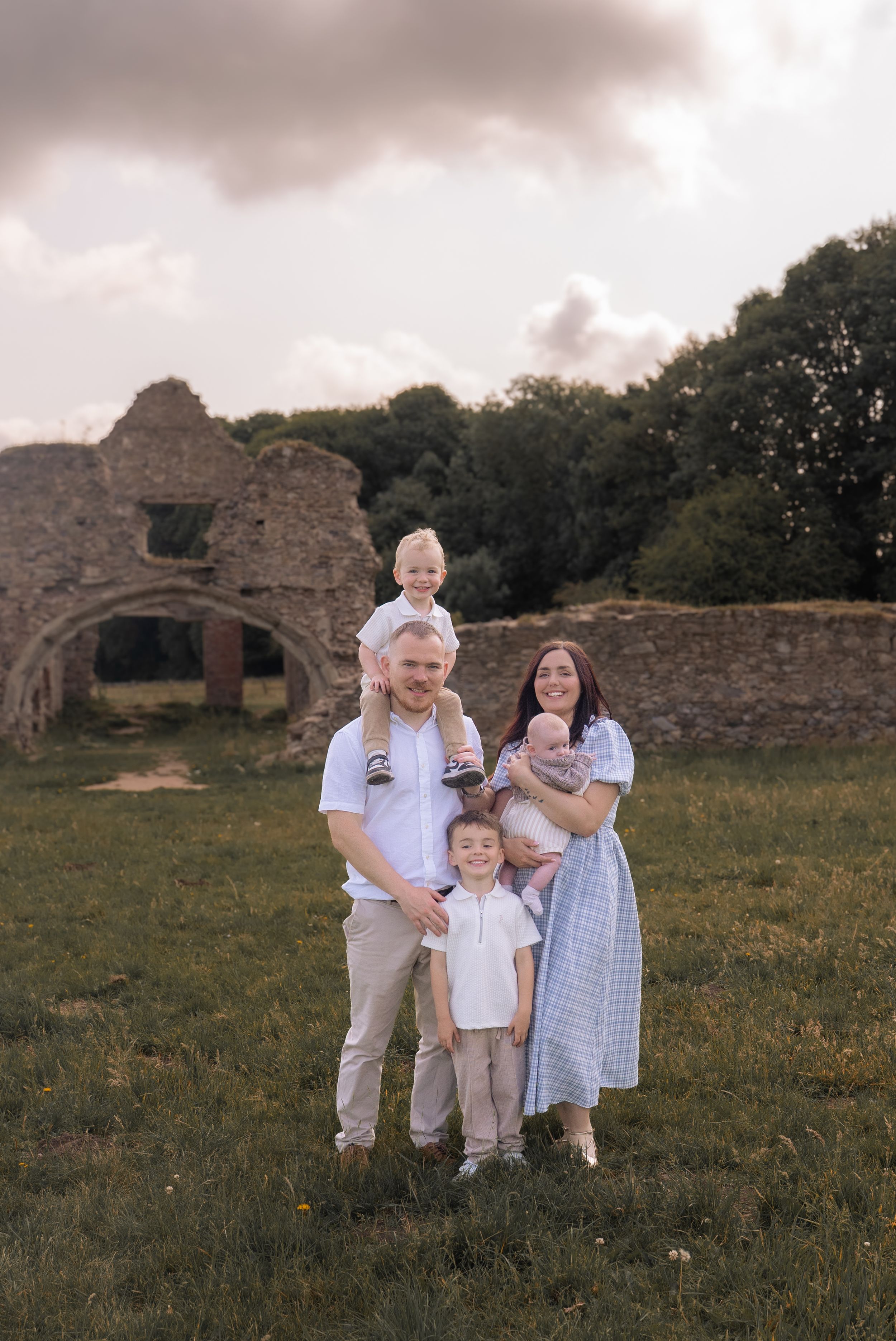 A family enjoys a summer evening together near old stone ruins in a grassy field.