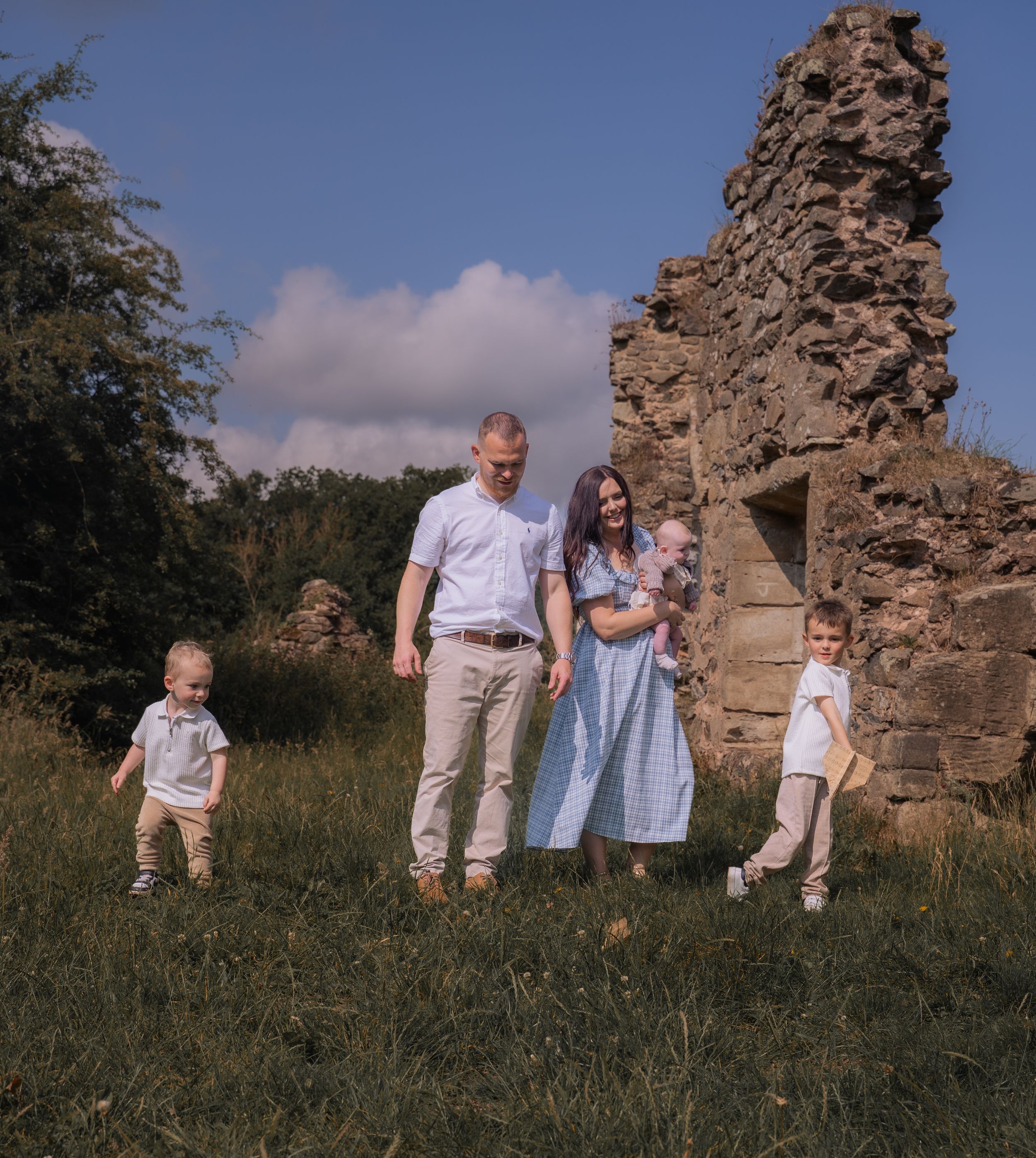 A family stands together near ancient stone ruins in a grassy field on a sunny summer day.