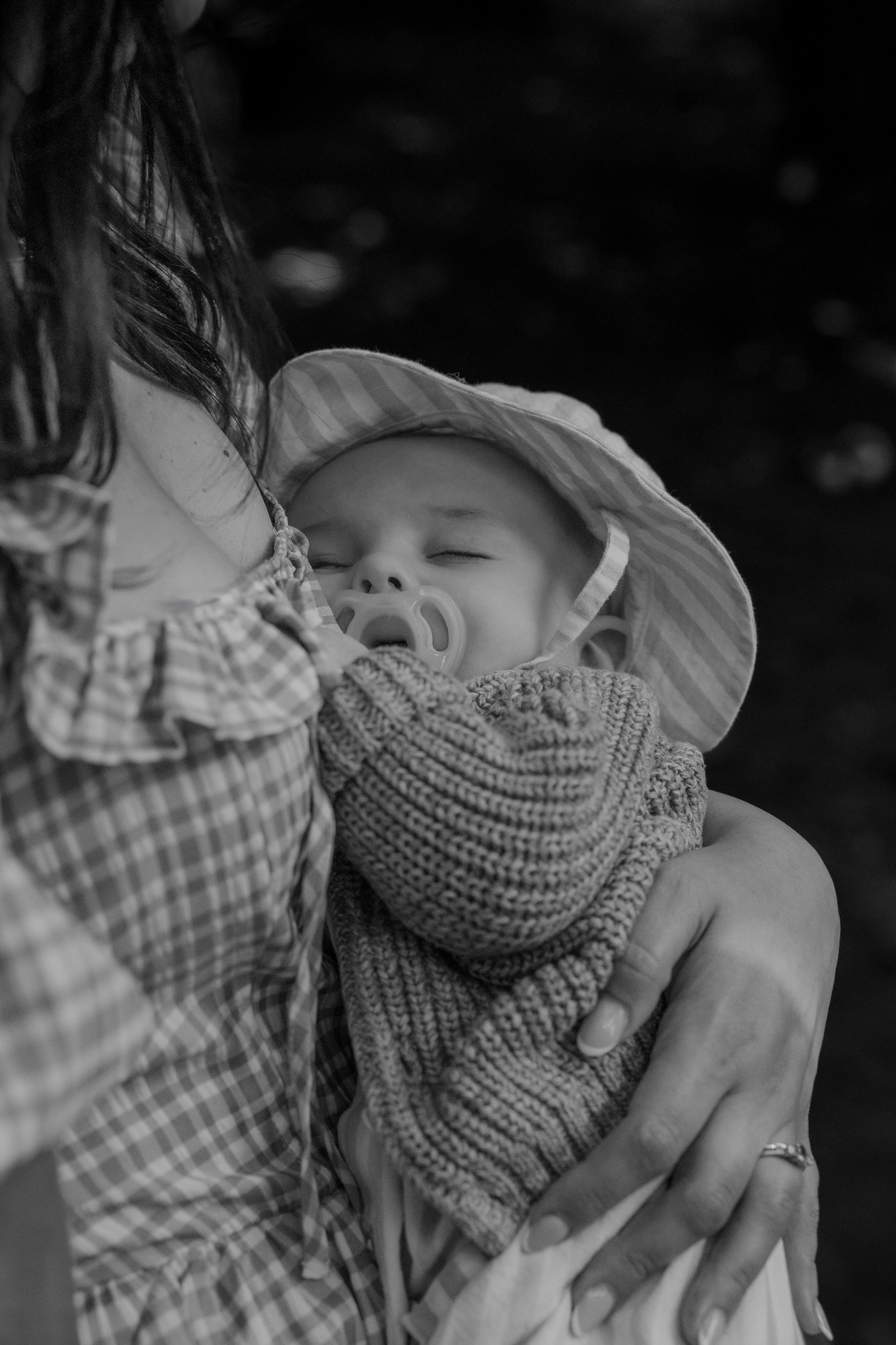 Black and white photo of a parent cradling a sleeping baby wrapped in a knit scarf.