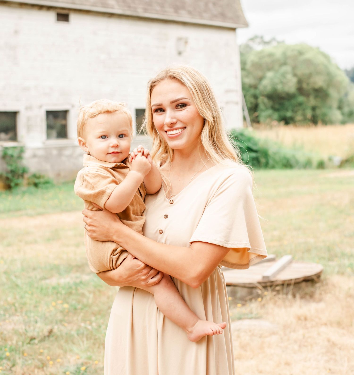 Family in matching peach-colored outfits poses together outdoors near rustic barn in warm sunlight.