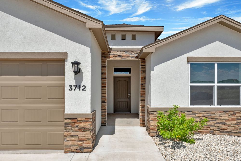 Modern beige stucco home exterior with stone accents, tan garage door, and desert landscaping under blue sky.