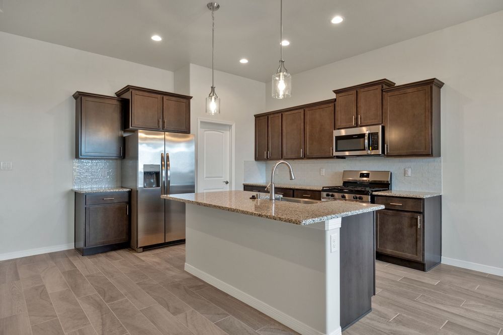 Modern open concept kitchen with dark wood cabinets, stainless steel appliances, and recessed lighting in new construction home.
