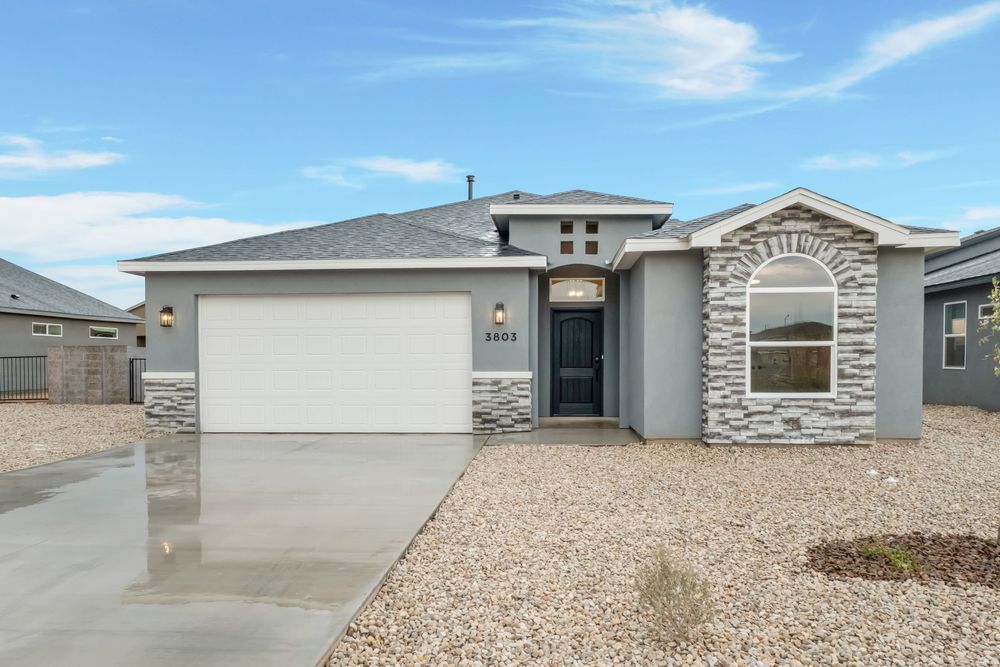 Modern desert home exterior with stone accents, beige stucco walls, and xeriscape landscaping in the front yard.