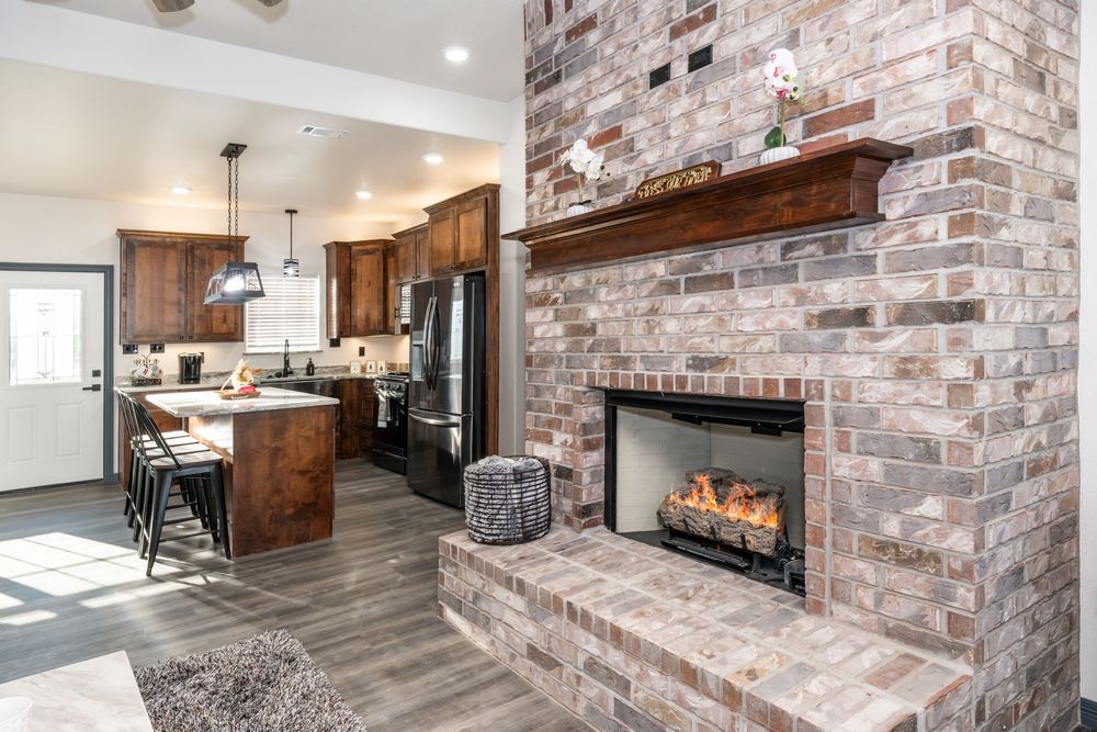 Modern kitchen and living area with exposed brick walls, wood beams, and gray flooring in an open concept layout.
