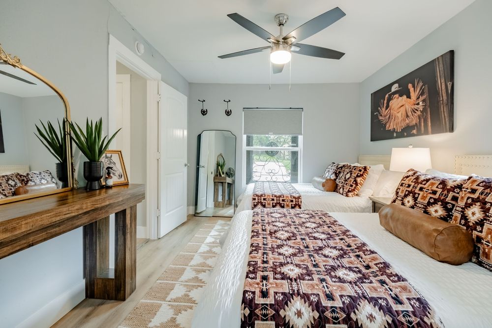 Modern bedroom with ceiling fan features burgundy patterned bedding, rustic console table, and decorative wall art.