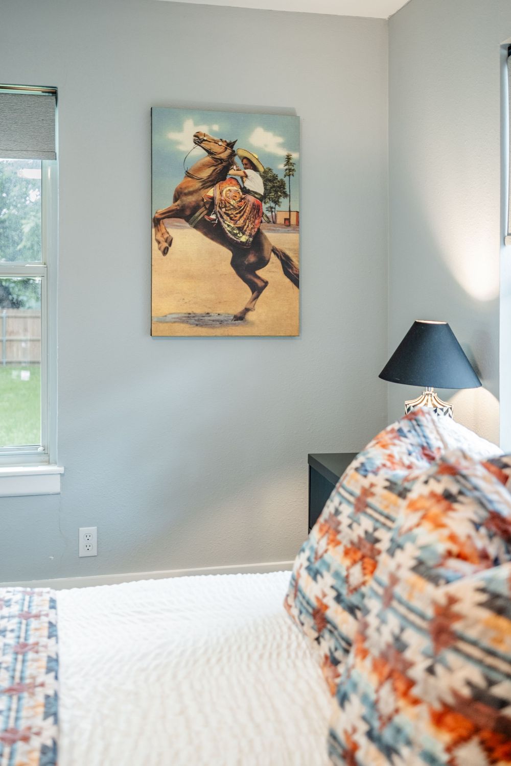 Light blue bedroom walls feature a western-themed artwork above a white bed with a patterned orange and white comforter.