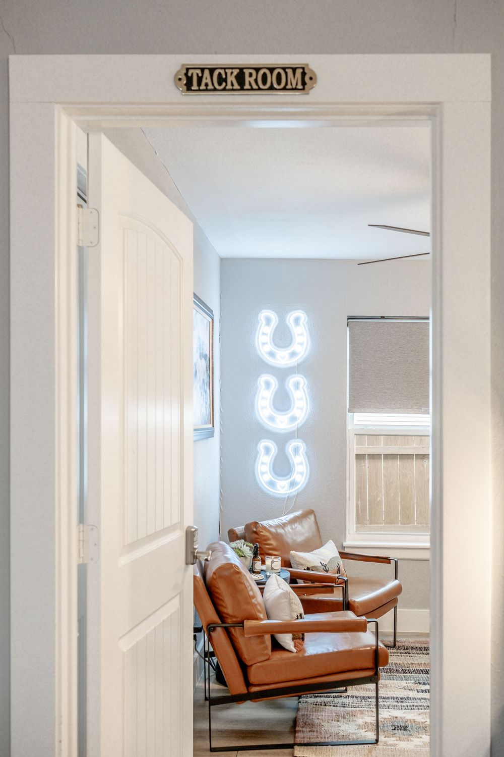 Modern tack room with brown leather chairs and glowing neon horseshoe signs mounted on white walls.