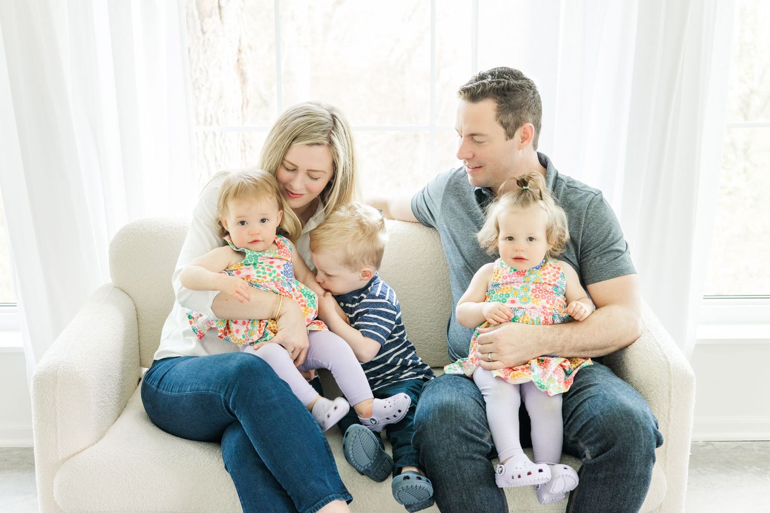 Family sitting together on white couch in coordinated casual outfits.