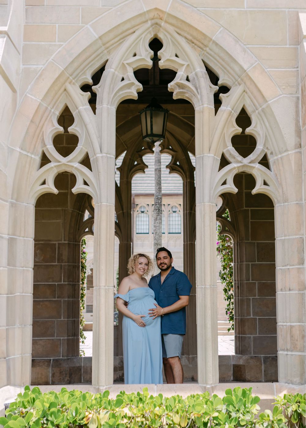Gothic arched colonnade with ornate stone details and tropical landscaping.