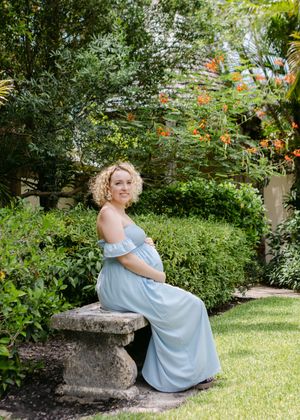A woman in a blue dress poses gracefully on stone benches in a garden setting.
