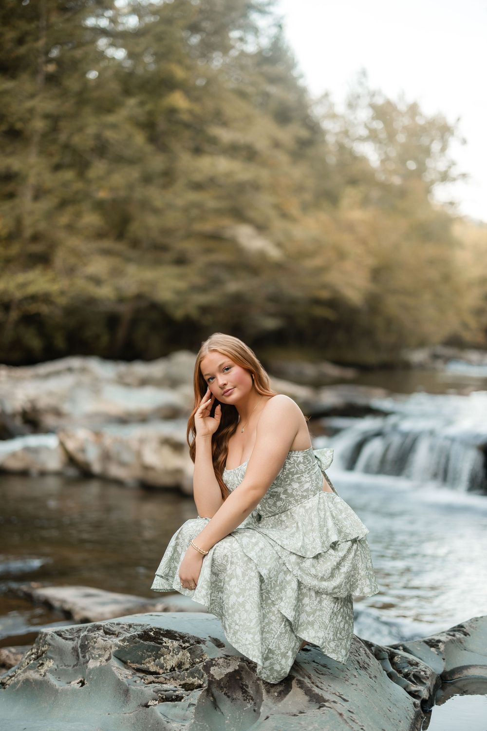 A dreamy photoshoot by a cascading waterfall features a mint green dress against natural rock formations and flowing water.