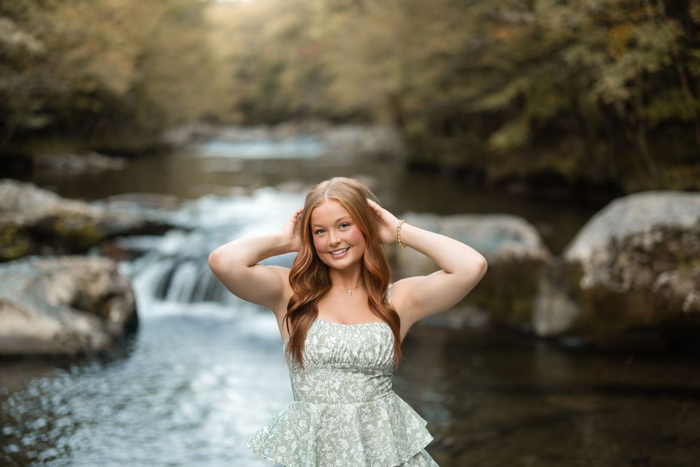A flowing white dress contrasts beautifully against dark rocks and water in a scenic outdoor photoshoot.