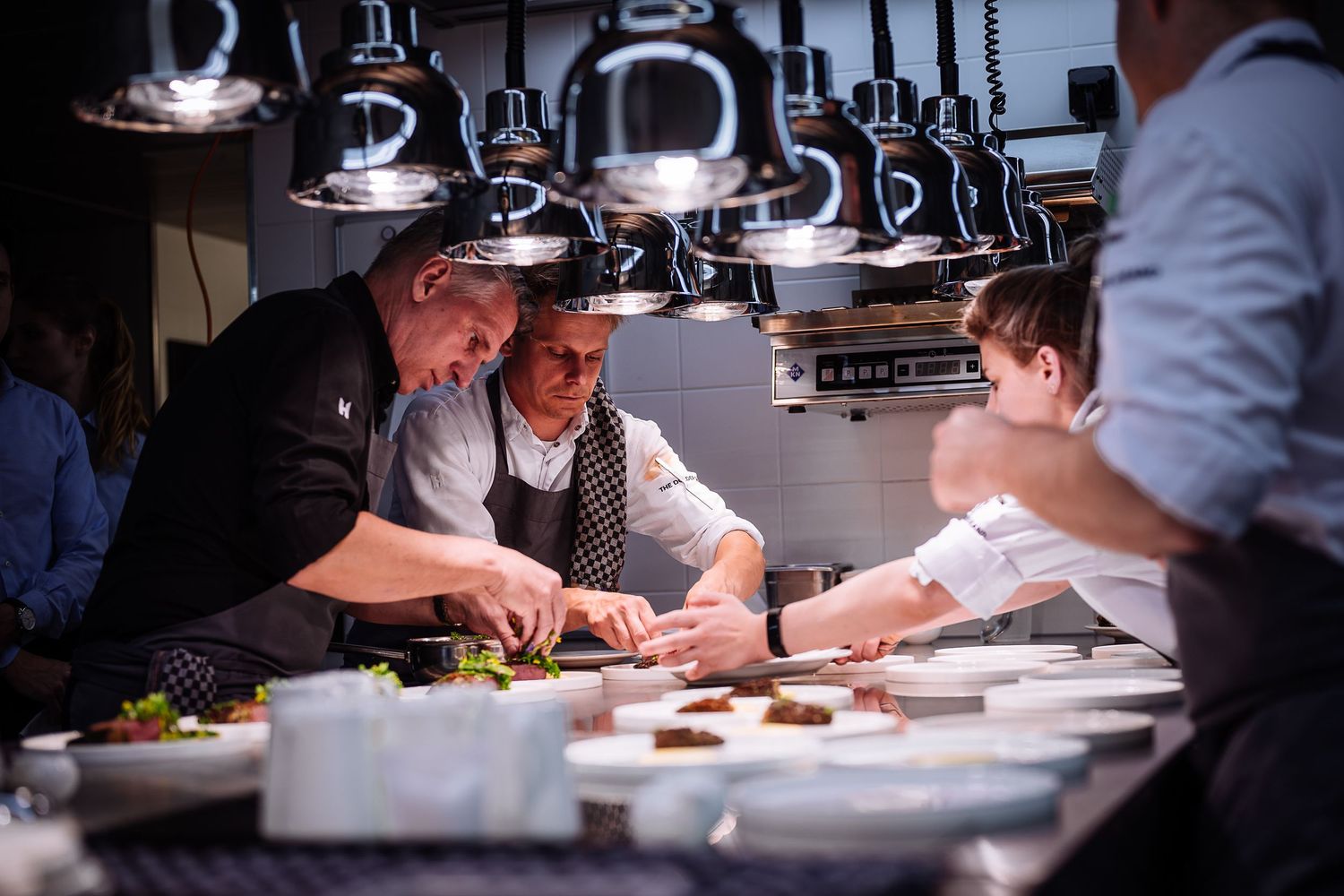 Professional chefs working in a dimly lit commercial kitchen preparing dishes with precision.