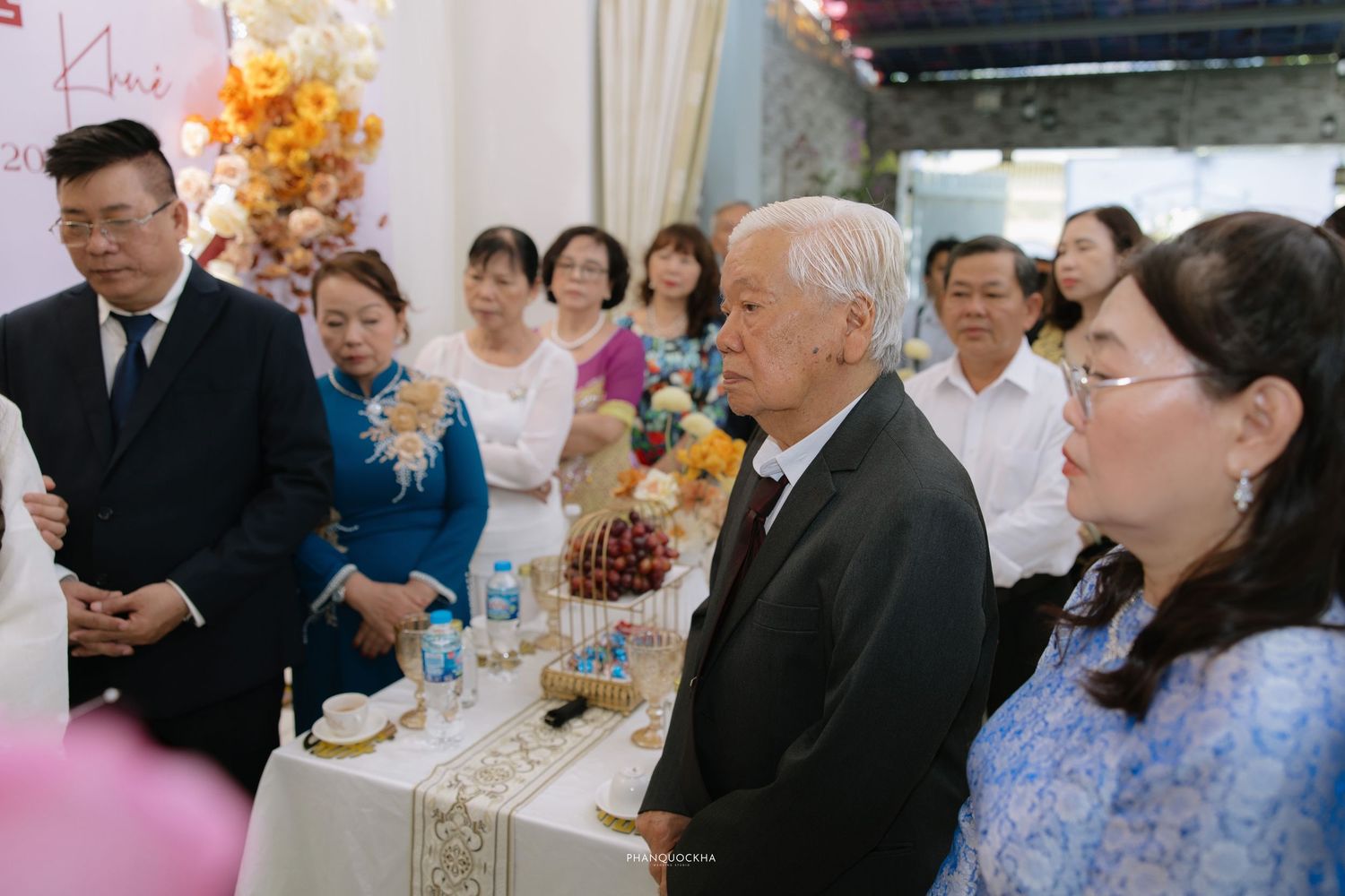 Elderly guests and family members gather around a decorated table at a Vietnamese wedding reception.