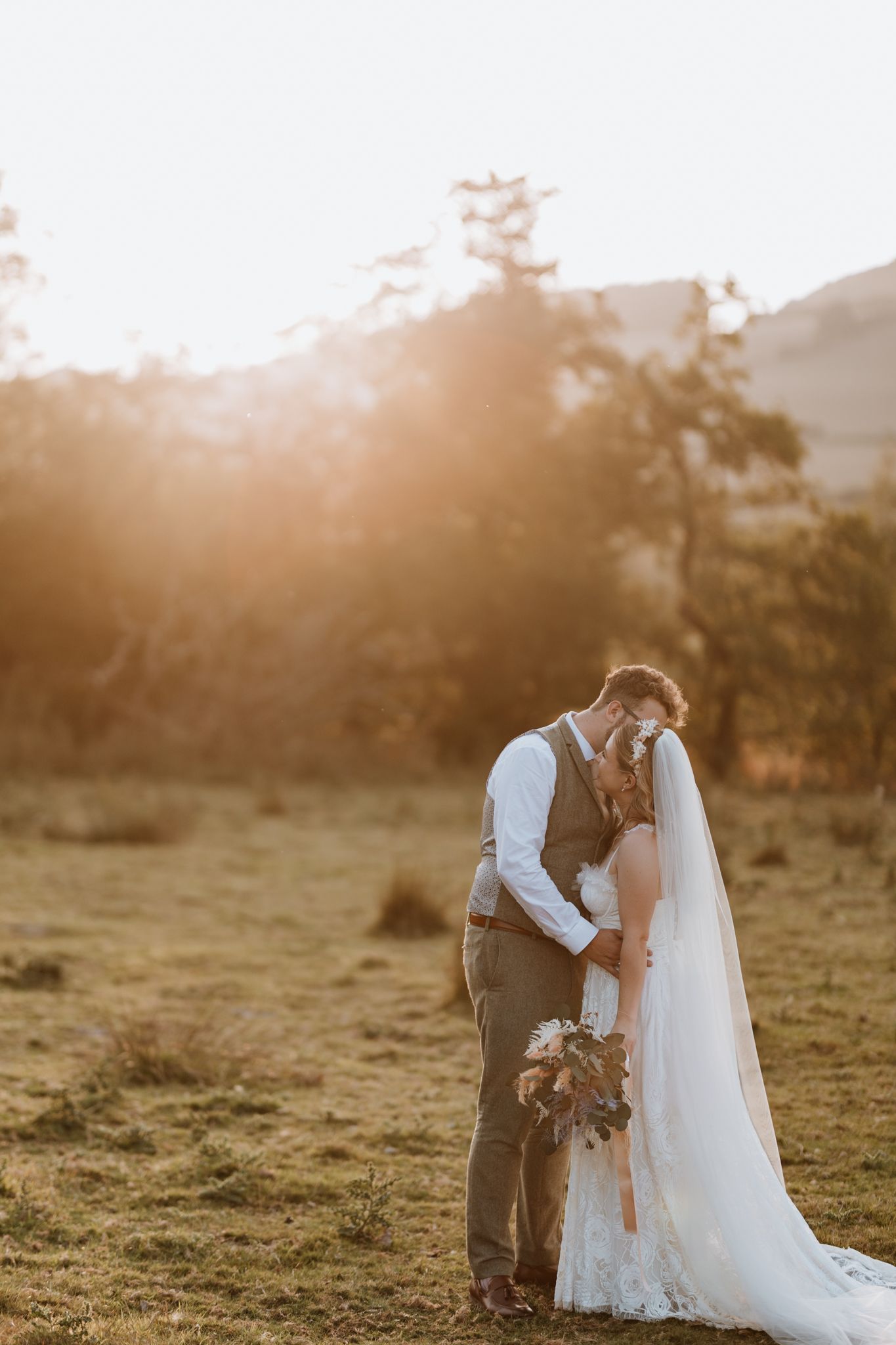 A newly married couple embraces in a golden sunlit meadow at sunset during their wedding at Wilde Lodge