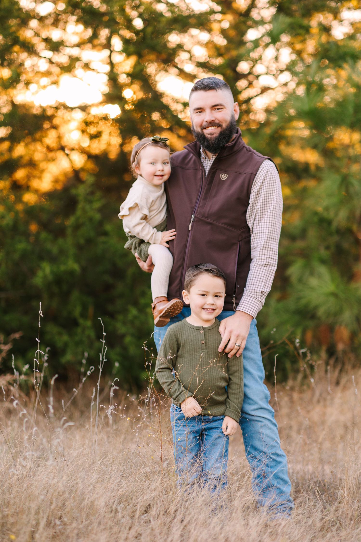 A loving family enjoys a warm autumn sunset together in a field of tall grass while wearing casual clothing.