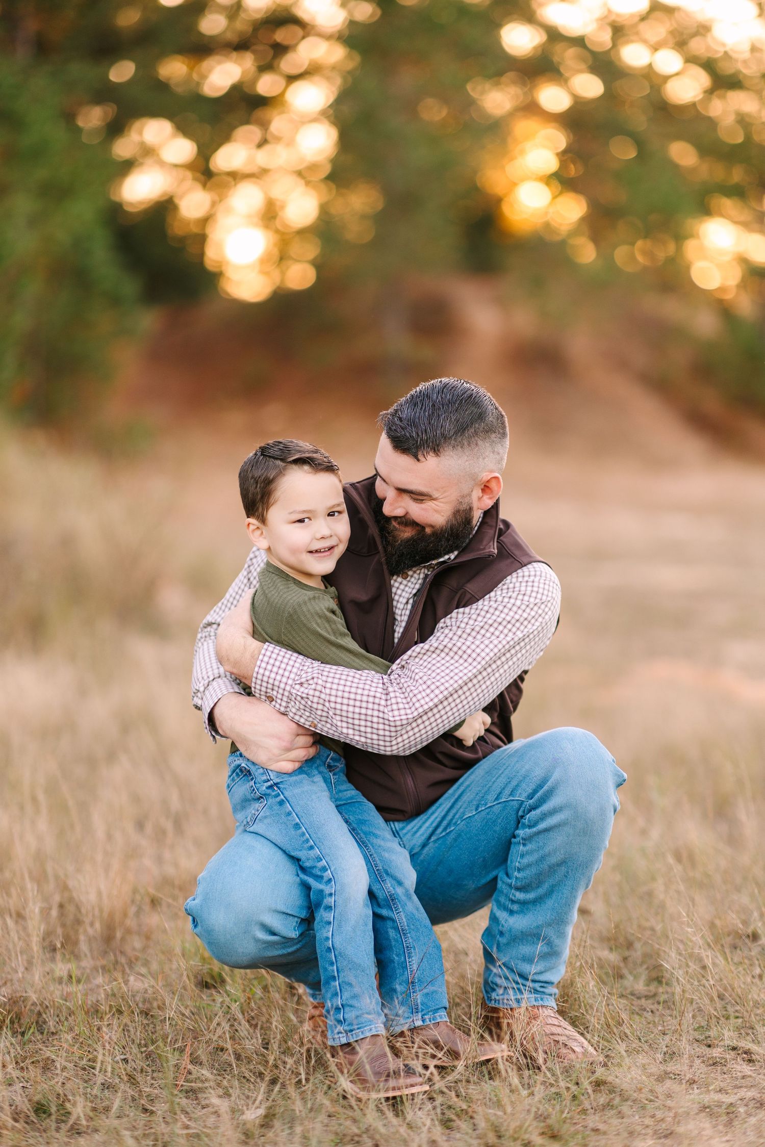 A tender family moment captured at sunset in a grassy field with beautiful golden bokeh lighting in the background.