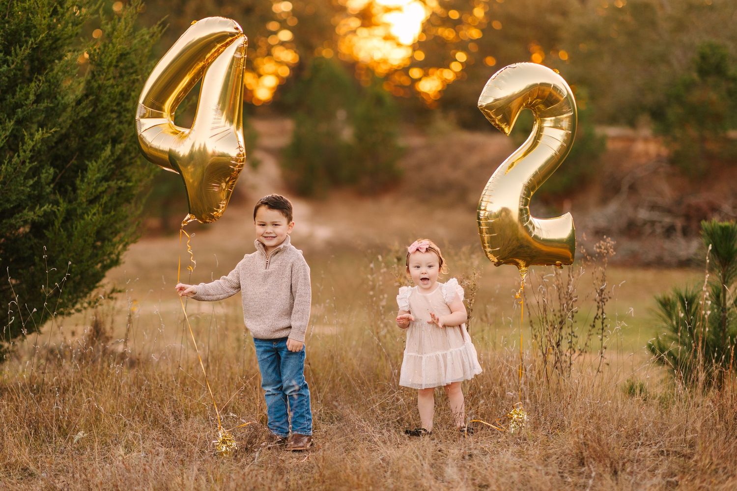 Gold number balloons float in a grassy field during sunset creating a magical scene.