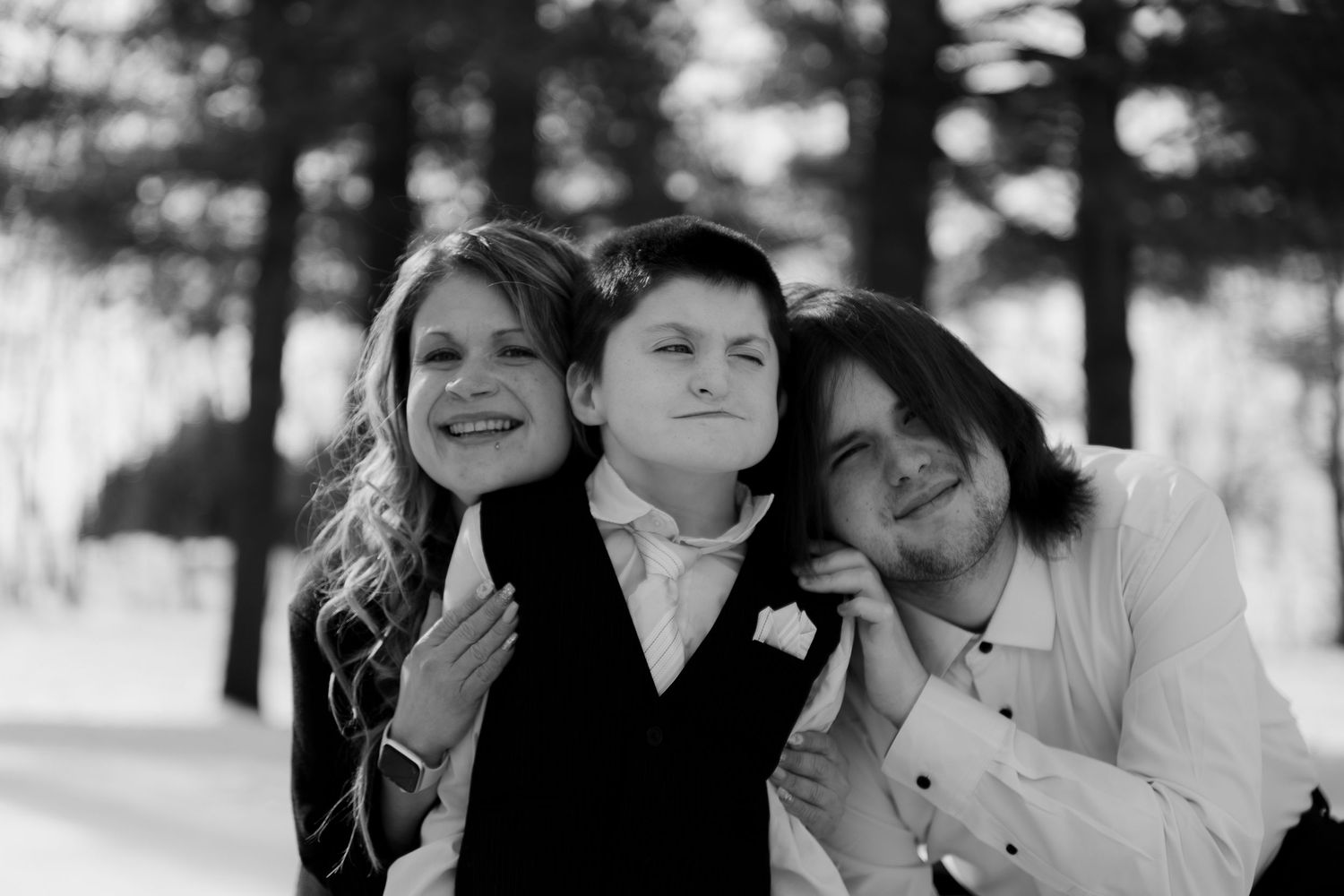 Three people pose closely together for a black and white portrait outdoors.