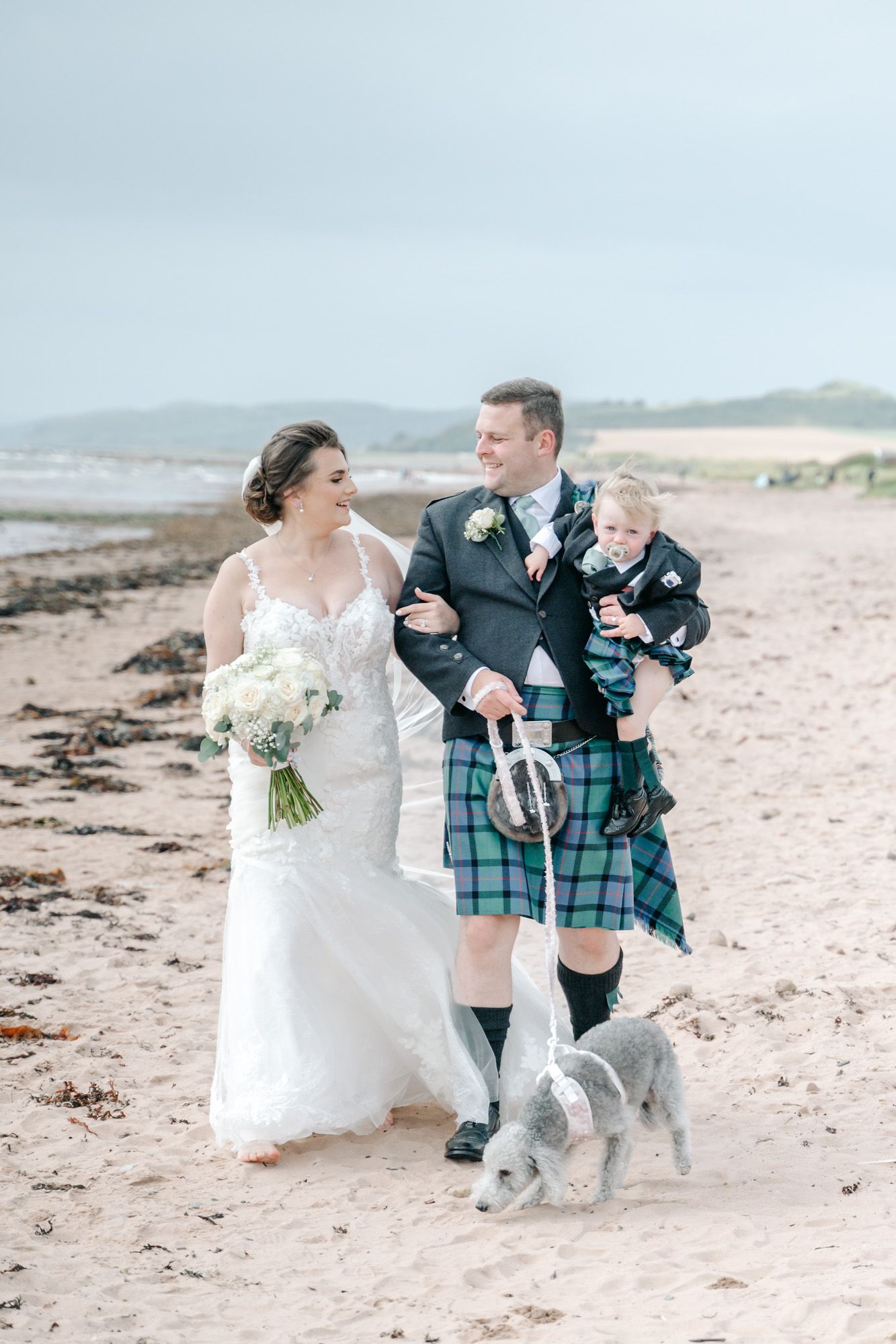 Wedding party poses playfully on beach with traditional Scottish kilts and white bridal gown.