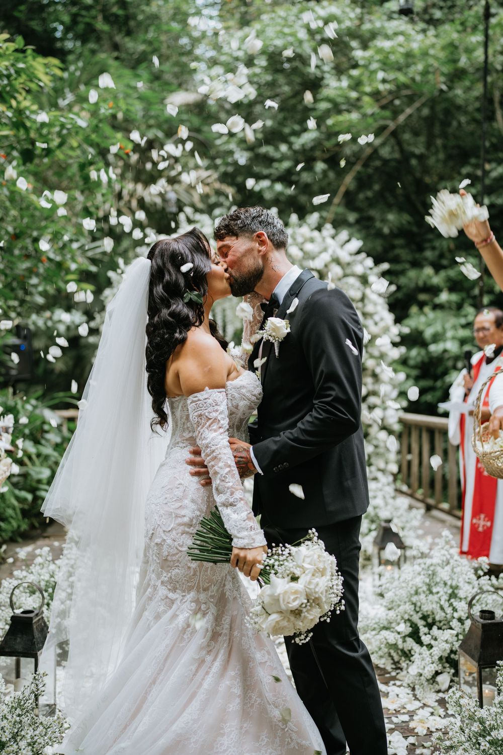 Romantic wedding ceremony moment under cascading white floral arrangements in garden setting.
