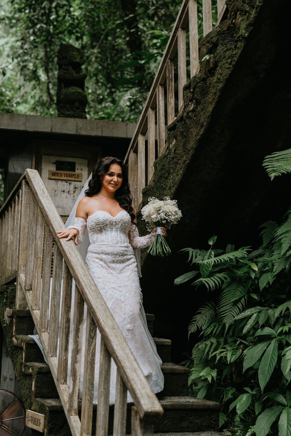 A lace wedding dress captured in a natural woodland setting with wooden stairs.