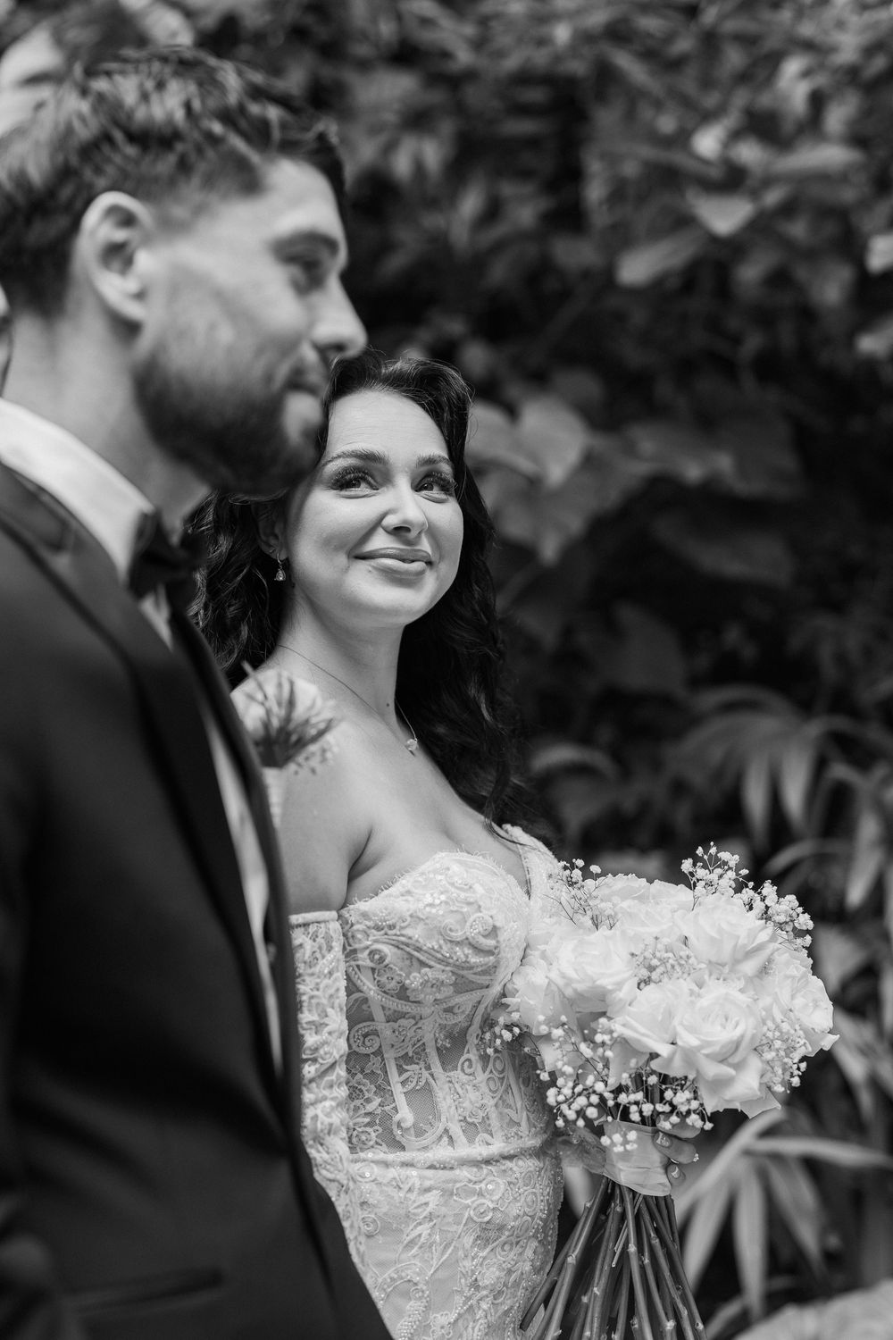 A black and white portrait of a couple sharing an intimate moment in a garden setting.