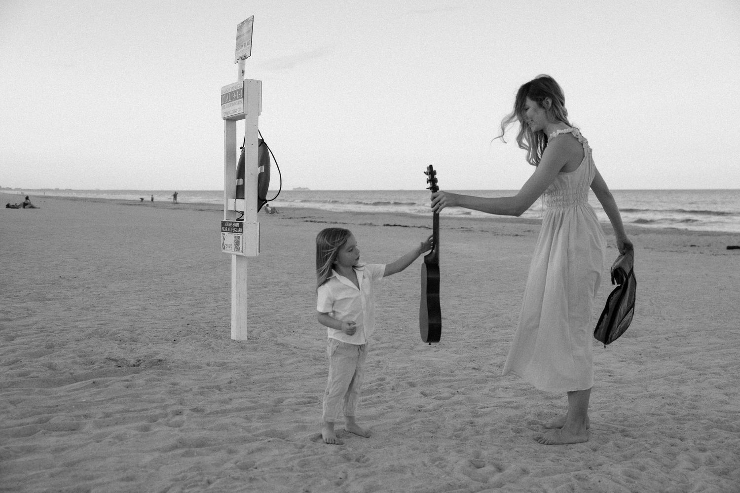 Black and white beach scene with couple and cross silhouette against ocean backdrop.