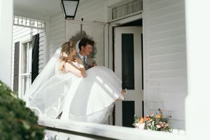 A flowing white wedding dress billows in the breeze on a classic white porch during an outdoor photoshoot. East Coast wedding photographer