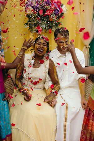 Joyful wedding celebration with flower petals being tossed against a yellow backdrop. Luxury Estate Wedding Photographer in NC