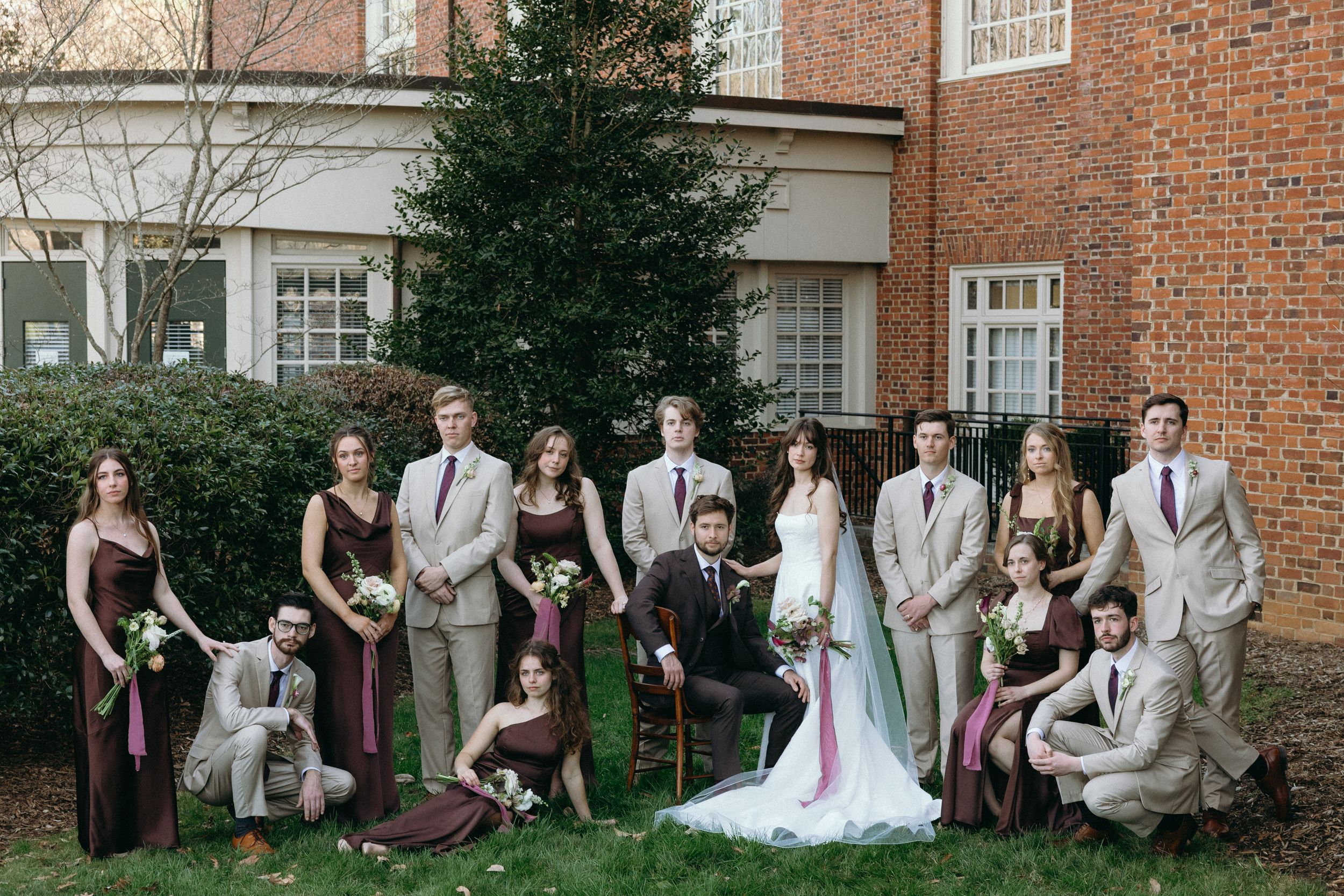 Wedding party poses playfully in front of red brick building during outdoor photo session.
