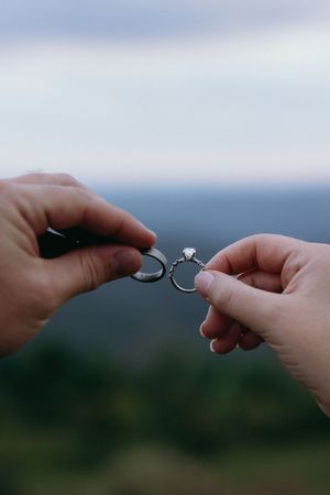 Hands exchange rings against blurred mountain landscape backdrop. Luxury Estate Wedding Photographer in NC