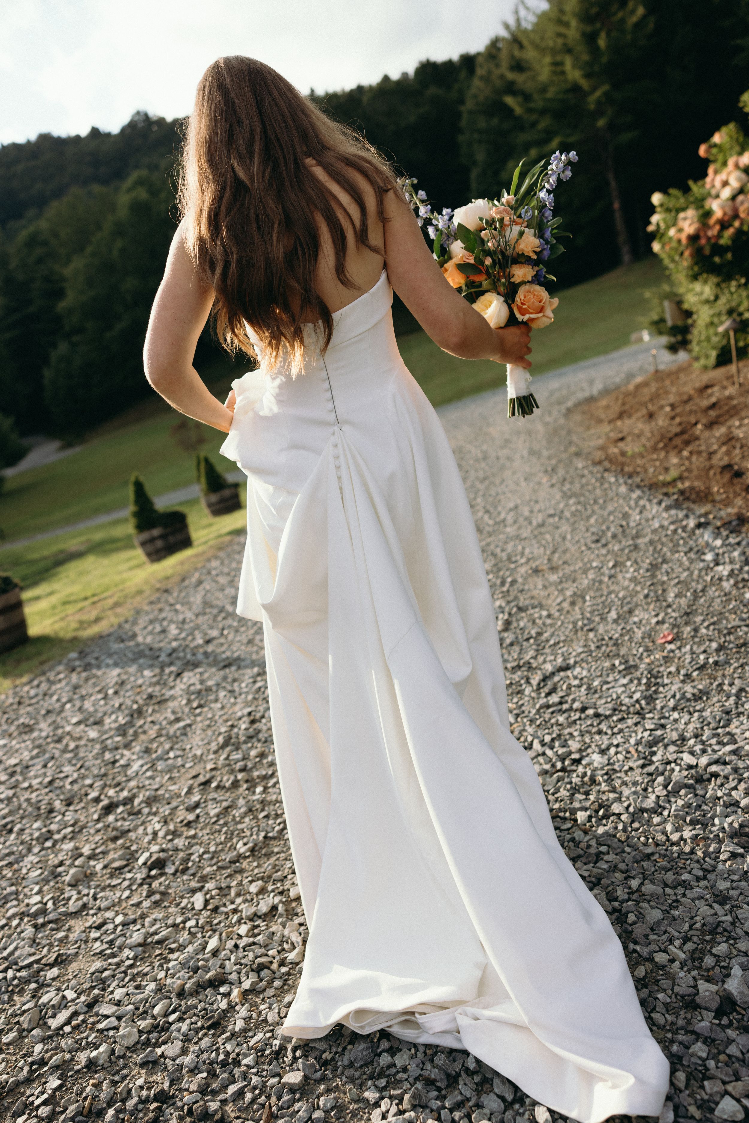 Flowing white wedding dress photographed on a gravel path with mountain scenery. Luxury Estate Wedding Photographer in NC