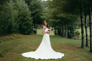 Elegant white wedding dress with a flowing train photographed outdoors among trees. East Coast luxury wedding photographer
